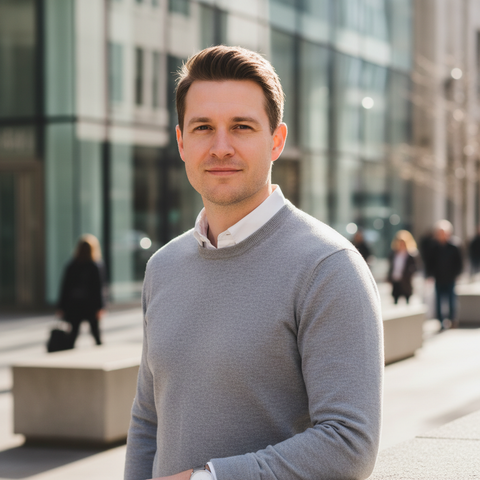 Professional portrait of Michael Reed, a project manager, smiling in a light gray sweater outdoors against a blurry modern city background
